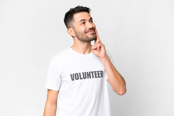 Junger freiwilliger kaukasischer Mann über isoliertem weißen Hintergrund, der eine Idee denkt, während er aufschaut - Foto, Bild