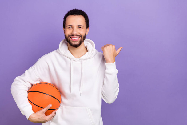 Photo de beau mec bras tenir basket doigt direct espace vide ad isolé sur fond de couleur violette. - Photo, image