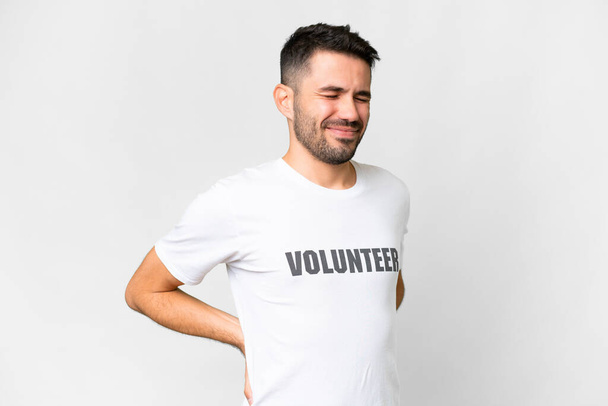 Jonge vrijwilliger blanke man over geïsoleerde witte achtergrond die lijdt aan rugpijn voor een inspanning hebben gedaan - Foto, afbeelding