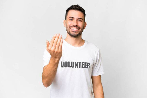 Young volunteer caucasian man over isolated white background inviting to come with hand. Happy that you came - Fotografie, Obrázek