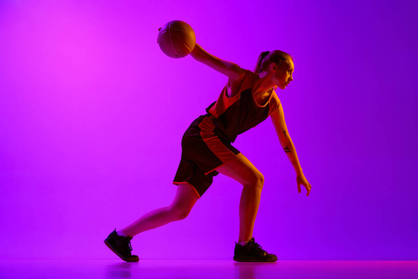 Young girl, concentrated female basketball player in motion, dribbling ball, training against white studio background. Concept of professional sport, hobby, healthy lifestyle, action and motion - 写真・画像