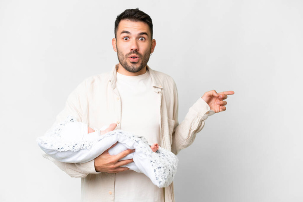 Young caucasian father with her newborn baby over isolated background surprised and pointing side - Foto, afbeelding