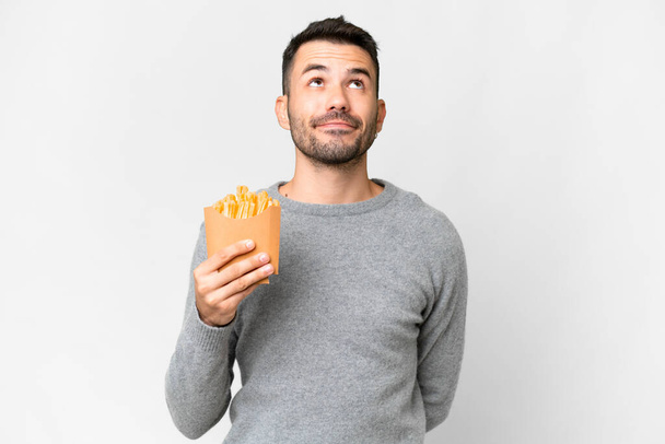 Jonge blanke man met gebakken chips over geïsoleerde witte achtergrond en omhoog kijkend - Foto, afbeelding