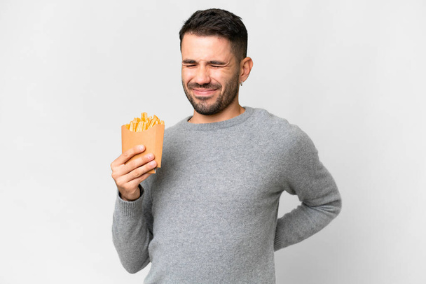Joven hombre caucásico sosteniendo patatas fritas sobre fondo blanco aislado que sufre de dolor de espalda por haber hecho un esfuerzo - Foto, imagen