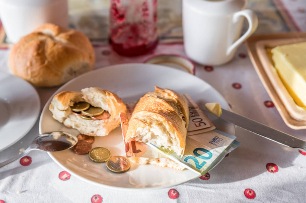 Ontbijttafel met ontbijt van koffiemelk en boter en broodjes bedekt met euromunten en -biljetten op bord, Duitsland - Foto, afbeelding
