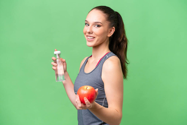 Mladá běloška žena přes izolované pozadí s jablkem a s lahví vody - Fotografie, Obrázek