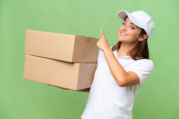 Delivery caucasian woman holding boxes isolated on green chroma background pointing back - Photo, Image