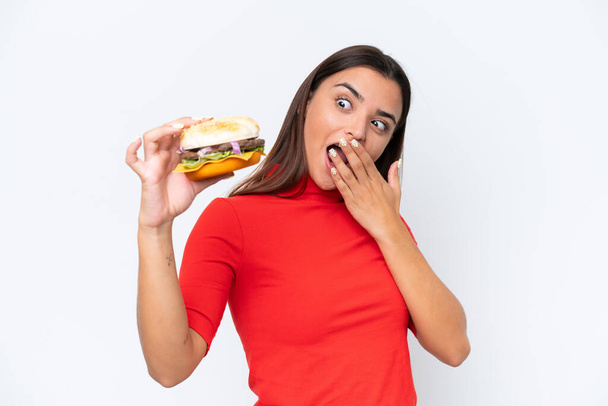 驚きとショックを受けた表情で白い背景に隔離されたハンバーガーを保持若い白人女性 - 写真・画像