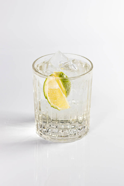 Gin és tonik koktél mély pohárban, citrommal és jéggel díszítve. Fehér alapon elszigetelve. - Fotó, kép