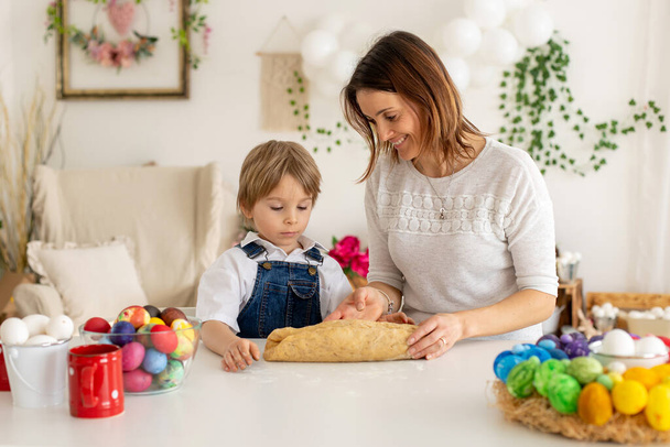 Little blond toddler child with young mother, preparing dough for easter brioche buns, sweet easter bread with nuts and dry fruits - Photo, image