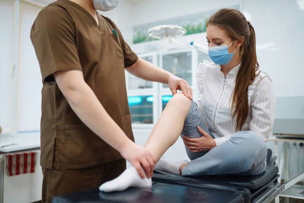 Patient visits a doctor after suffering a leg injury. The doctor examines the patient, examines the picture of the patient. Osteopathy, chiropractic, leg correction, rehabilitation. - Foto, imagen