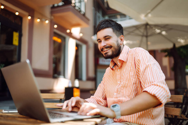 Smiling young man working in a cafe on the street with a laptop and phone. Freelance business concept. Business, blogging, freelancing, education concept. Modern lifestyle. - Φωτογραφία, εικόνα