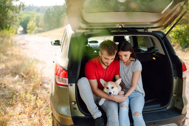 Lovely young couple with a dog sits in the back seat of a car. Happy man with a woman and his beloved dog travel together. Concept of active lifestyle, travel, weekend, relax. - Foto, imagen