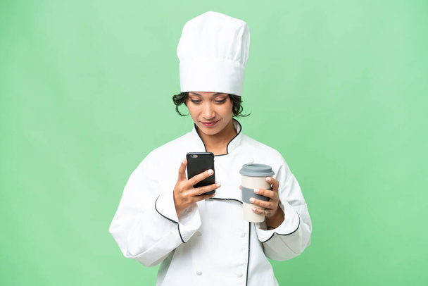 Young chef Argentinian woman over isolated background holding coffee to take away and a mobile - Фото, зображення