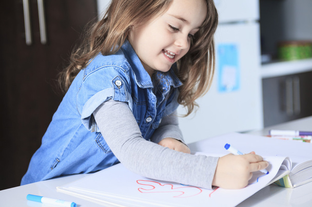 Cheerful little girl colouring at the table at home in kitchen - Foto, Imagem