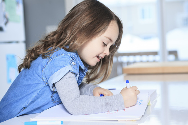 Cheerful little girl colouring at the table at home in kitchen - Photo, Image