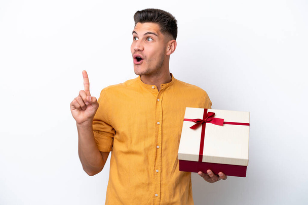 Young caucasian man holding a gift isolated on white background intending to realizes the solution while lifting a finger up - Photo, image