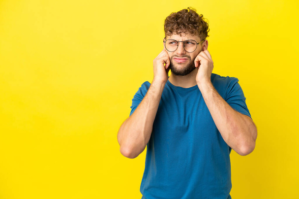Young handsome caucasian man isolated on yellow background frustrated and covering ears - 写真・画像