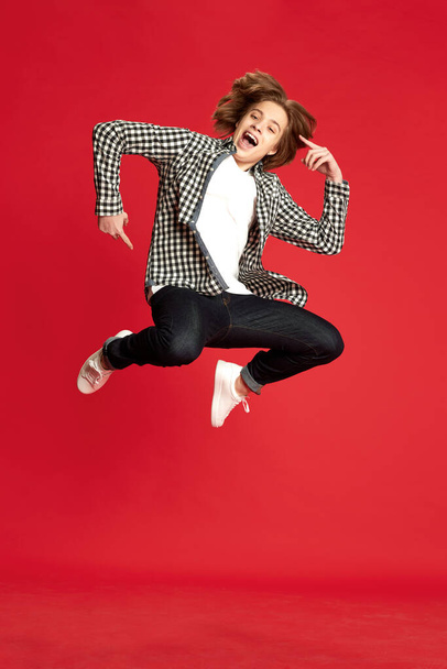 Exam passed, joy. One young guy, student wearing casual style clothes dancing over red studio background with pleasure. Concept of education, human emotions, mood, psychological condition, beauty, ad - Fotografie, Obrázek