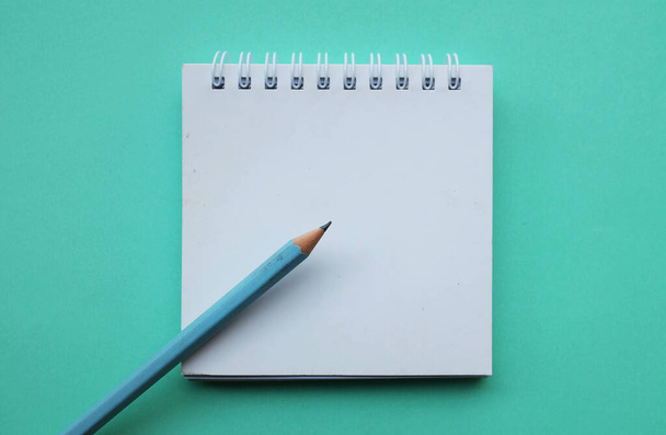 close-up en plat leg een potlood op witte spiraalvormige notitieblok op een tafel groene pastel achtergrond. onderwijs- en bedrijfsconcept schoolbenodigdheden en kantoorwerk - Foto, afbeelding