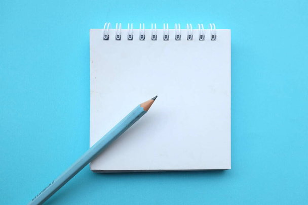close-up en plat leg een potlood op witte spiraalvormige notitieblok op een tafel blauwe pastel achtergrond. onderwijs- en bedrijfsconcept schoolbenodigdheden en kantoorwerk - Foto, afbeelding