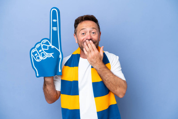 średnim wieku kaukaski sportowy fan człowiek odizolowany na niebieskim tle szczęśliwy i uśmiechnięty pokrycie usta z ręki - Zdjęcie, obraz