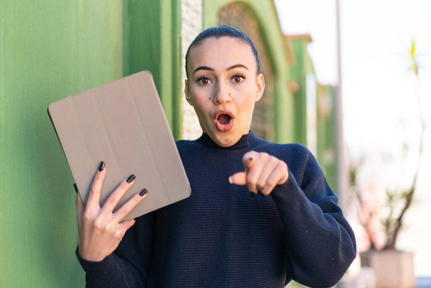 Young moroccan girl holding a tablet at outdoors surprised and pointing front - Foto, afbeelding