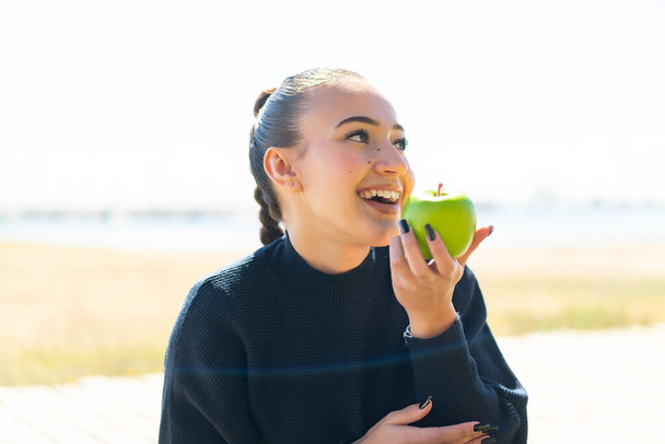 młody marokańska dziewczyna na zewnątrz gospodarstwa jabłko z szczęśliwy ekspresja - Zdjęcie, obraz