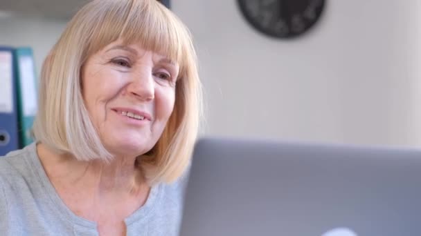 Een oudere vrouw heeft een videogesprek op kantoor, ze is energiek en in een goed humeur. Werken met een computer op oudere leeftijd. 4k video - Video