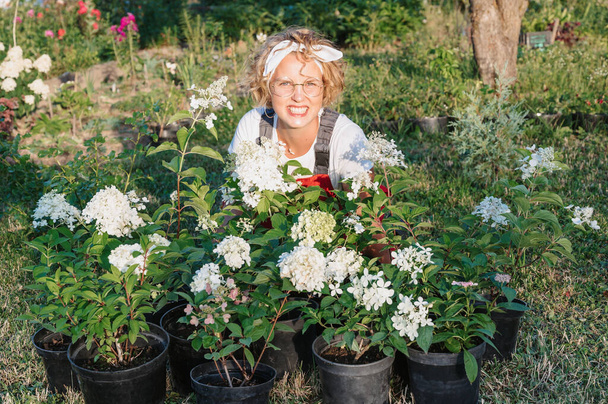 Portré egy boldog vidám női virágos-kertész egy hortenzia virágcserép a szabadban. Kertészkedés és virágtermesztés. Növekvő virágok az otthoni kertben. - Fotó, kép