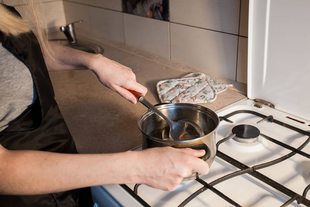 A girl boils eggs in a metal pan on a white gas stove in the kitchen. Image for your creative decoration or design. - Photo, image