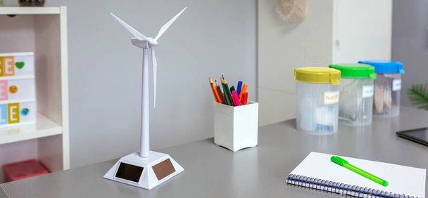 Primer plano del molino de viento solar y contenedores de basura selectivos sobre el escritorio en el aula ambiental vacía. Concepto de educación ecológica. - Foto, imagen