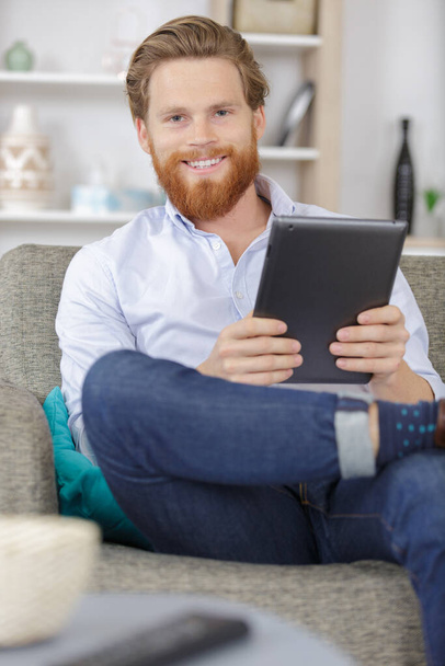 happy man on the sofa and holding tablet in hands - Foto, imagen