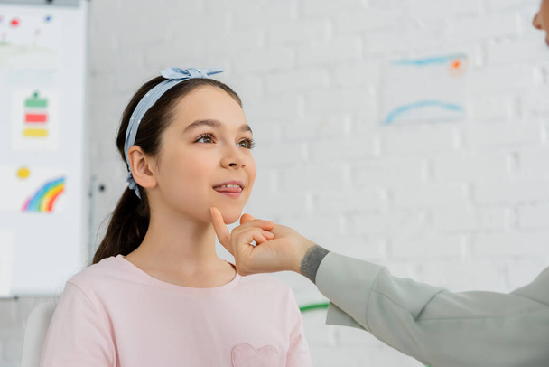 Speech therapist toccare mento di pupilla preadolescente durante la lezione in sala di consultazione  - Foto, immagini