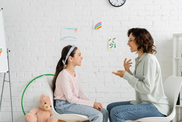 Vue latérale de l'orthophoniste et de l'enfant parlant pendant les cours dans la salle de consultation  - Photo, image