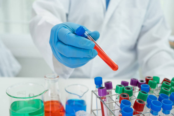 Bilimsel kimya laboratuvarında kırmızı renkli sıvı çözeltisi olan konik cam şişeyi elinde tutan bilim adamı.. - Fotoğraf, Görsel