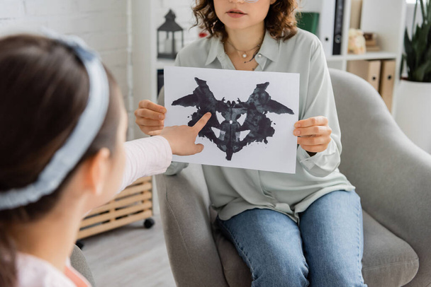 Wazig meisje wijst naar Rorschach test in de buurt van psycholoog in spreekkamer  - Foto, afbeelding