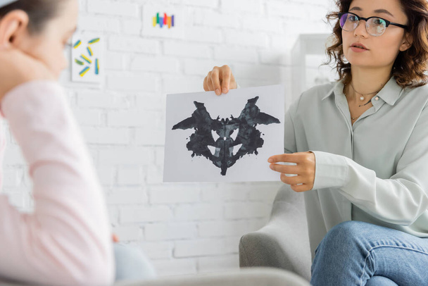 Psychologist holding Rorschach test near blurred preteen girl in consulting room  - Фото, изображение