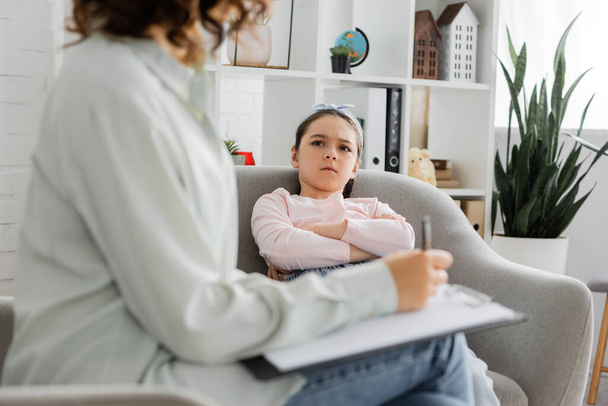 Chica enojada mirando psicólogo borroso con portapapeles en la sala de consulta  - Foto, imagen