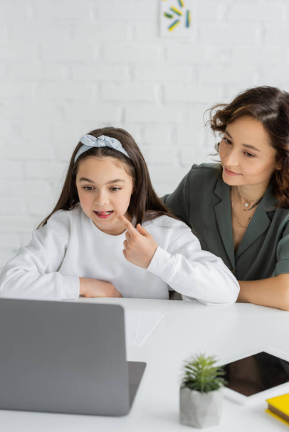 Preteen girl pointing at mouth during speech therapy online lesson near mom at home  - Valokuva, kuva