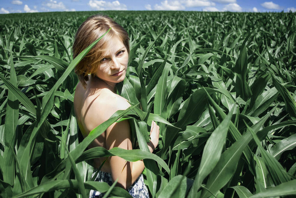 Genç bir kadın yemyeşil bir mısır tarlasında duruyor. Sırtüstü uzanmış, temiz hava soluyor ve doğanın tadını çıkarıyor. - Fotoğraf, Görsel