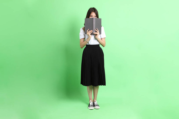 The young school girl with uniform standing on the green background. - Photo, Image