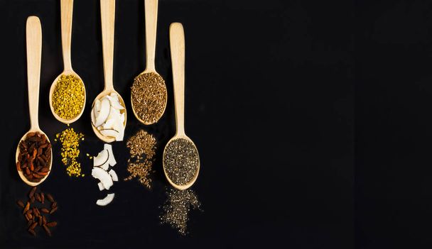 Set of natural superfood in the wooden spoons on the black background.Copy space. Top view. - Φωτογραφία, εικόνα