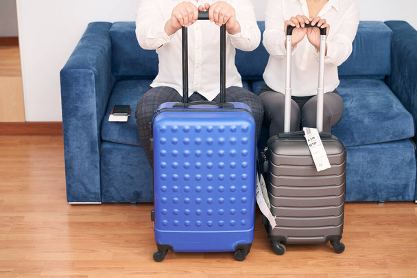 Cropped photo of tourist couple with trolley suitcases sitting on comfortable sofa - Foto, Imagen
