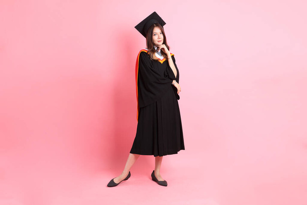 Азиатка в выпускном платье, стоящая на розовом фоне. - Фото, изображение