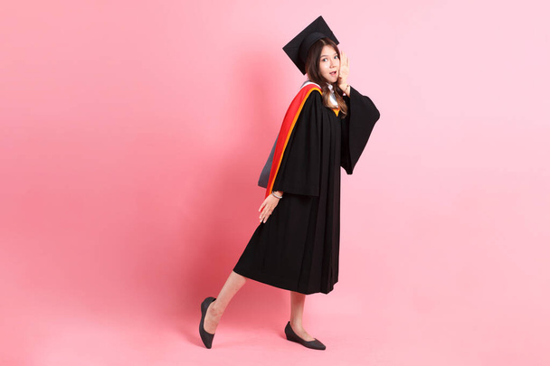 de aziatische vrouw in afstuderen jurk staande op de roze achtergrond. - Foto, afbeelding