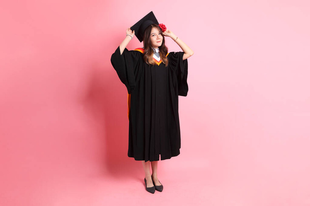 de aziatische vrouw in afstuderen jurk staande op de roze achtergrond. - Foto, afbeelding