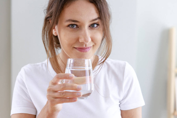 Young woman drinking water at home. Health benefits of drinking enough water concepts.  - Photo, image