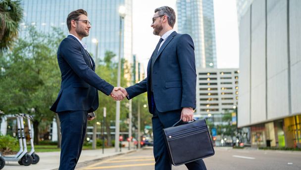 Business man shaking hands. Two businessmen handshake outdoor. Handshake business people. Handshake of two business man outdoor. Business man wearing modern suit in building city background - 写真・画像