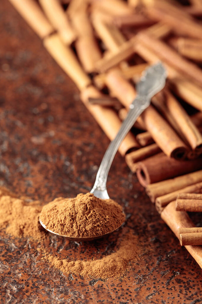 Cinnamon powder in a spoon and cinnamon sticks on a brown background.  - 写真・画像